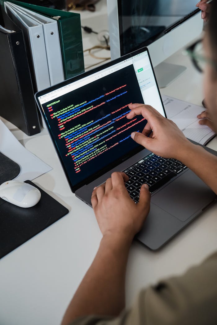 gallery-01 Close-up of a programmer pointing at a colorful code script on a laptop in an office setting.