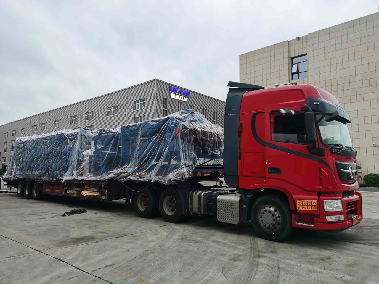 services-03 Red truck with large covered cargo in an industrial area, overcast day.