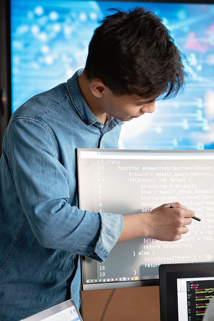 gallery-02 Asian male programmer writing code on a computer monitor in an office setting.