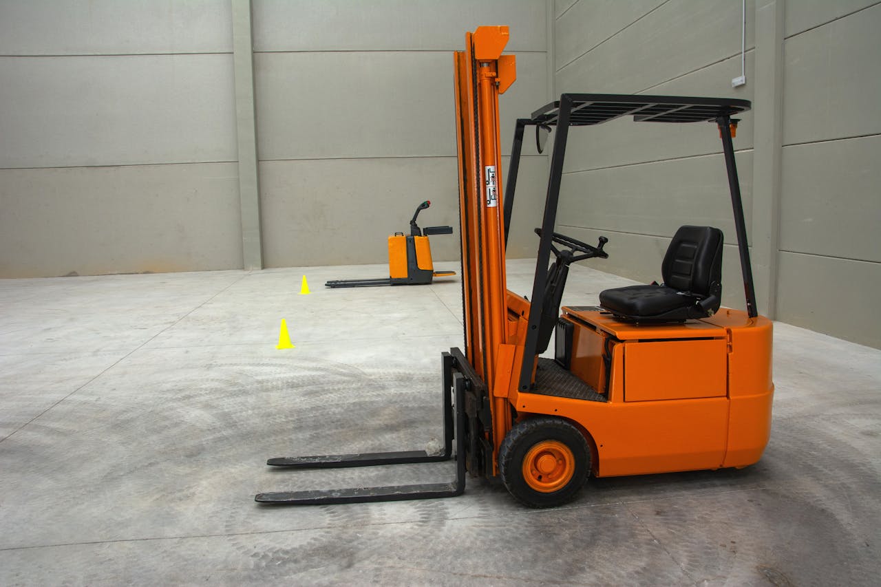portfolio-01 An orange forklift in a spacious warehouse with concrete floors and minimal equipment.