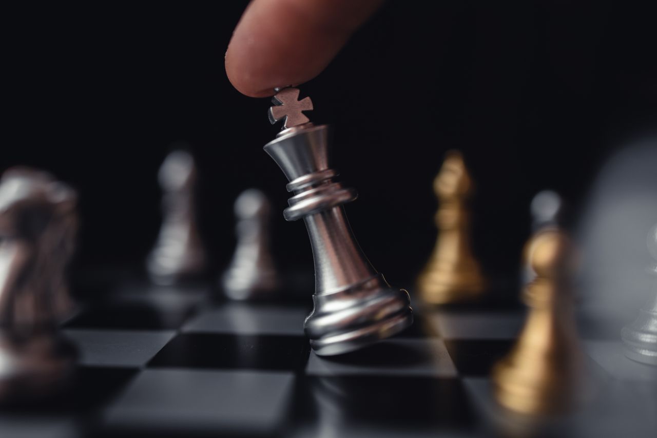 Intense focus on a hand moving a silver king chess piece in strategic play.